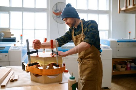 Foto de Joven articulador masculino que fija la construcción de madera para el interior de diseño o el montaje de muebles utilizando diferentes herramientas sobre el fondo del taller - Imagen libre de derechos