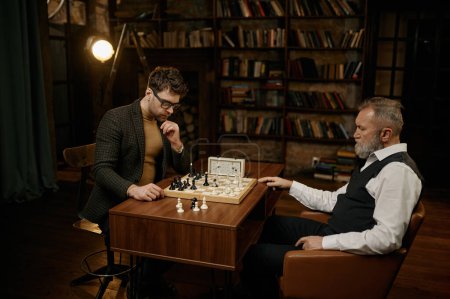Téléchargez les photos : Les joueurs d'échecs concentrés organisent un match de compétition dans la salle de la bibliothèque. Homme âgé et jeune homme jouant jeu en utilisant chronomètre pour mesurer le temps - en image libre de droit