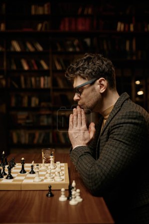 Photo for Serious young man looking thoughtfully at chessboard pieces. Logic game next move planning concept - Royalty Free Image