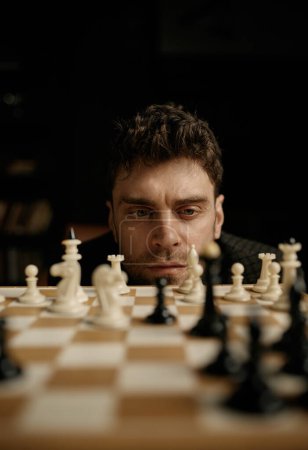 Photo for Face portrait of thoughtful young man player considering chess piece position on board planning strategic move. Selective focus and closeup view - Royalty Free Image