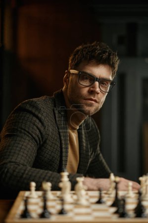 Téléchargez les photos : Portrait de jeune homme joueur d'échecs assis à table avec échiquier - en image libre de droit