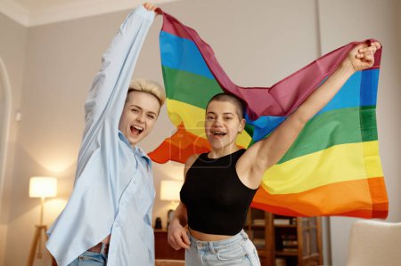 Téléchargez les photos : Les jeunes amants du couple LGBTQ se sentent fiers et se préparent pour le défilé de tolérance tenant le drapeau au-dessus de la tête et criant - en image libre de droit