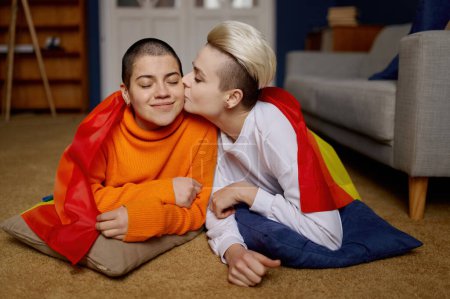 Foto de Retrato de pareja lesbiana cariñosa posando junto con la bandera multicolor del arco iris sobre los hombros. Lgbt mujer besando a su novia. Concepto de aceptación, amor y orgullo - Imagen libre de derechos
