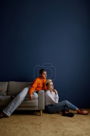 Téléchargez les photos : Affectueux couple lesbienne romantique se reposer à la maison en regardant le verre de fenêtre. Dreamy lgbt femme pleine longueur portrait - en image libre de droit