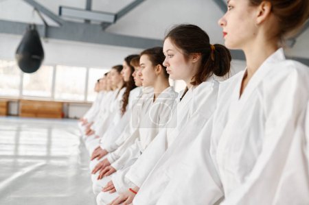 Photo for Young aikido students wearing kimono sitting in row. Teenage sports children waiting for start of group lesson or listening to their coach during training - Royalty Free Image