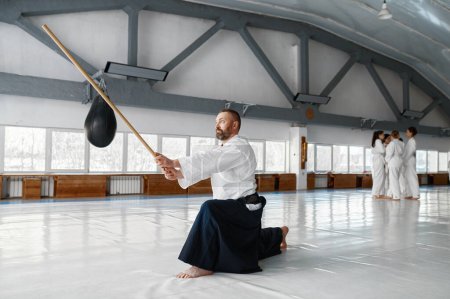 Téléchargez les photos : Formation de maître aikido mature confiante et forte avec épée japonaise bokken debout dans la pose de combat - en image libre de droit