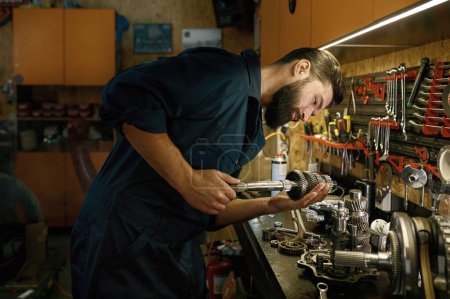 Photo for Male mechanic character working in garage on weekend. Man technician engaged on inspection of repaired wheel shaft spare part for motorcycle - Royalty Free Image