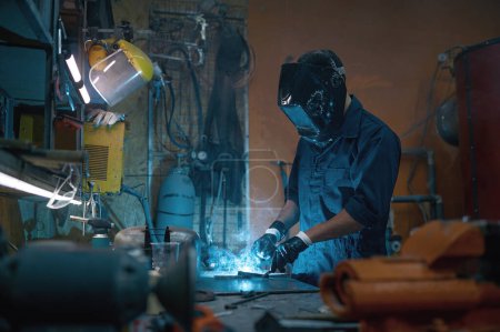 Foto de Reparador profesional con casco protector y overol trabajando con soldadura en taller de motocicletas - Imagen libre de derechos