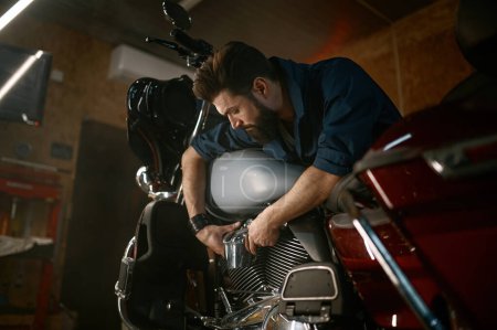 Téléchargez les photos : Mécanicien masculin travaillant dans le garage et la réparation de moto personnalisée. Concept d'atelier créatif authentique - en image libre de droit