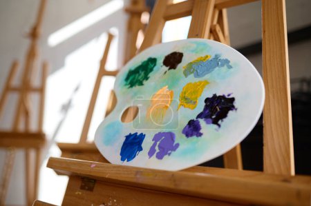 Photo for Acrylic paints colors mix on plastic palette lying on wooden easel, selective focus. Art studio workshop, creative workspace for artist - Royalty Free Image