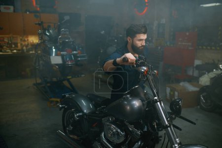 Foto de Auto mecánico de la motocicleta móvil en el stand de reparación en el taller de garaje. Hombre técnico preparando el vehículo para la restauración - Imagen libre de derechos