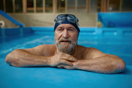 Téléchargez les photos : Portrait d'un aîné mature portant un chapeau et des lunettes de bain à la piscine. Un nageur barbu aux cheveux gris regardant la caméra. Concept de sport, mode de vie actif et retraite - en image libre de droit
