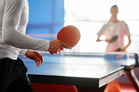 Selektive Fokussierung auf zwei sportliche Menschen, die in der Halle Tischtennis spielen. Freundschaftsspiel zwischen Männern und Frauen
