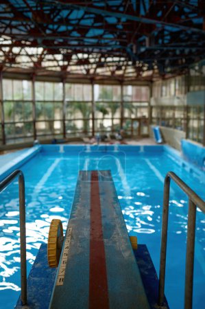 Téléchargez les photos : Planche de plongée à la piscine intérieure vide avec reflets de lumière dans l'eau bleue. Endroit confortable pour la formation - en image libre de droit