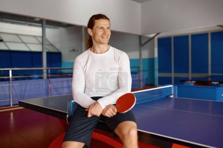 Photo for Satisfied sportsman having rest after training sitting on tennis table. Portrait of young man holding racket in hand - Royalty Free Image