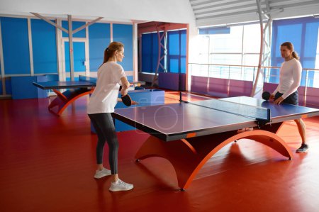 Foto de Hombre y mujer jugando al tenis de mesa en el interior. Instructor masculino enseñando a una estudiante en un club deportivo profesional - Imagen libre de derechos