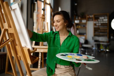Téléchargez les photos : Portrait de jeune femme heureuse peignant le pinceau sur toile à l'atelier pendant la classe de leçon d'art. Concept d'activité de loisirs créative - en image libre de droit