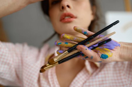 Foto de Retrato artístico de artista femenina creativa con enfoque selectivo en manos pintadas sucias sosteniendo manojo de pincel. Recortado primer plano de joven pintor - Imagen libre de derechos