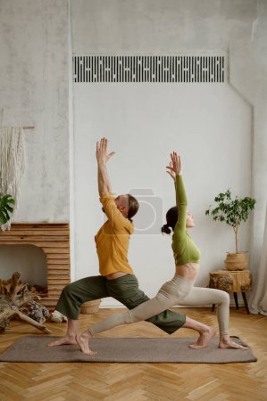 Photo for Young man and woman couple practicing yoga together standing in triangle pose. Healthy lifestyle and sport daily routine concept - Royalty Free Image