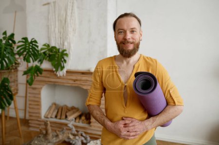 Téléchargez les photos : Portrait d'homme souriant heureux tenant tapis de yoga se préparer pour la pratique à la maison. La routine sportive active - en image libre de droit
