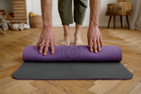 Photo for Fitness man folding exercise mat before yoga working out at home, cropped closeup view. Equipment for training - Royalty Free Image