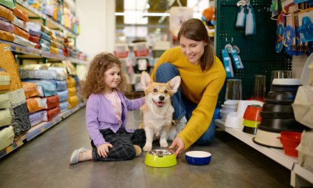 Feliz madre e hija alimentando a su perro corgi en la tienda de mascotas