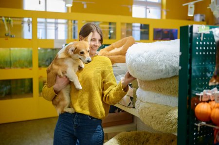Téléchargez les photos : Jeune femme souriante tenant un chien corgi sur les mains en choisissant un endroit doux pour dormir à l'animalerie - en image libre de droit