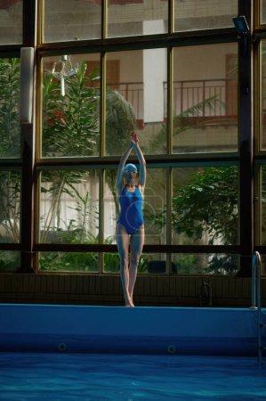 Foto de Mujer joven de pie junto a la piscina con las manos levantadas listas para saltar en la piscina. Concepto de entrenamiento deportivo y práctica de natación - Imagen libre de derechos