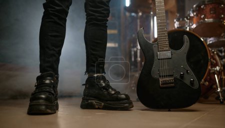 Photo for Cropped view on rocker feet legs on stage with electric guitar musical instrument. At rehearsal concept - Royalty Free Image