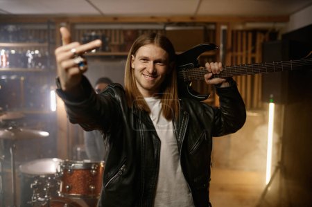 Photo for Rock musician holding electric guitar on shoulder gesturing fuck off middle finger gesture to camera. Bad expression, provocation and rude attitude concept - Royalty Free Image