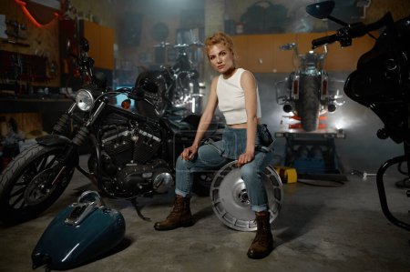 Photo for Young trendy blond woman mechanic at motorbike garage. Repair work and bike maintenance service - Royalty Free Image