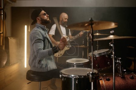Photo for Rock band performance. Focus on stylish male drummer beating music rhythm on drum with sticks - Royalty Free Image