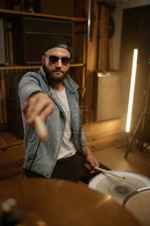 Photo for Stylish male drummer in trendy outfit and sunglasses pointing drumstick to camera. Music band repetition - Royalty Free Image