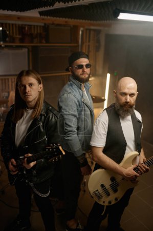 Foto de Retrato de banda de rock con guitarrista rockstar de diferentes edades mostrando expresividad a la cámara - Imagen libre de derechos