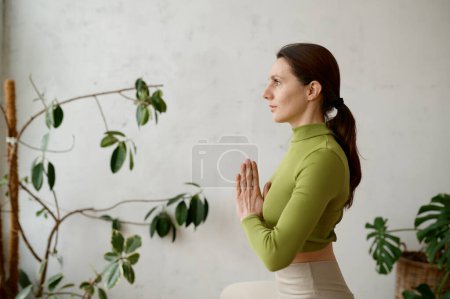 Téléchargez les photos : Portrait de vue latérale de la jeune femme pratiquant la technique de pleine conscience yoga assis en position lotus, respirant et méditant - en image libre de droit