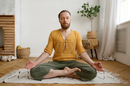 Foto de Deportivo hombre consciente meditando solo en casa apartamento. Tranquilo chico hipster calma practicando yoga en pose de loto en el interior tomados de la mano en mudra - Imagen libre de derechos