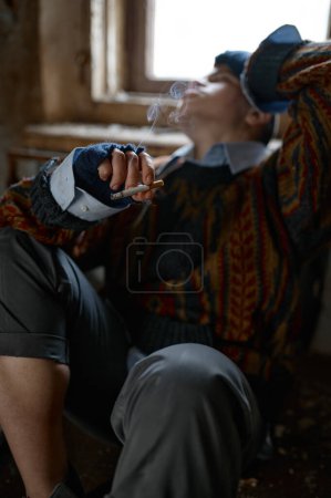 Foto de Chica con ropa vieja y sucia fumando cigarrillo, enfoque selectivo. Adolescente sin hogar desfavorecida - Imagen libre de derechos