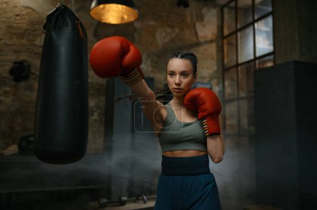 Photo for Portrait of young female boxer practicing punches wearing boxing gloves looking concentrated and confidently - Royalty Free Image