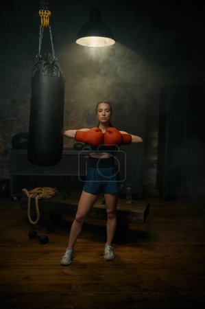 Téléchargez les photos : Portrait de belle femme sportive professionnelle en gants de boxe rouge posant dans un studio de gym - en image libre de droit