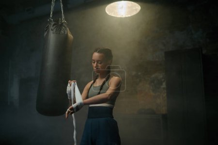 Téléchargez les photos : Femme forte athlète enveloppant ses mains avec des bandages de boxe. boxer féminin se préparant pour la pratique de l'exercice de combat et de kickboxing - en image libre de droit