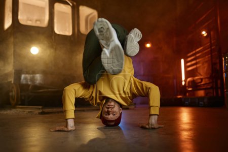 Téléchargez les photos : Jeune homme décontracté danseur freestyle debout sur la tête faisant acrobatie cascade sur fond de station souterraine urbaine - en image libre de droit