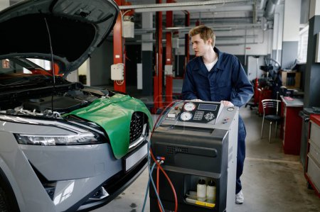 Foto de Reparador en el garaje del coche haciendo control y mantenimiento de aire acondicionado. Estación de servicio automática profesional - Imagen libre de derechos