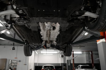Photo for Bottom view of raised car on lift in repair garage. Visible details and structure of suspension or elements of exhaust system - Royalty Free Image