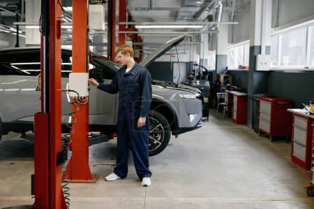 Foto de El hombre mecánico enciende el servicio automático de reparación de trabajo de elevación de automóviles que proporciona mantenimiento del motor - Imagen libre de derechos