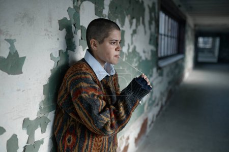 Photo for Portrait of homeless hipster teenager woman with short hair chewing gum looking aside. Poor teen girl wearing ragged clothes - Royalty Free Image