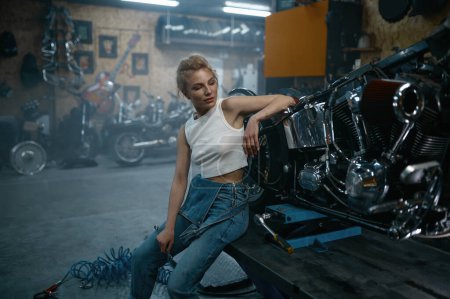 Téléchargez les photos : Jolie femme mécanicienne posant pour caméra au garage de moto. Réparatrice professionnelle à l'atelier authentique - en image libre de droit