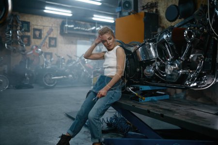 Téléchargez les photos : Jolie femme mécanicienne posant pour caméra au garage de moto. Réparatrice professionnelle à l'atelier authentique - en image libre de droit