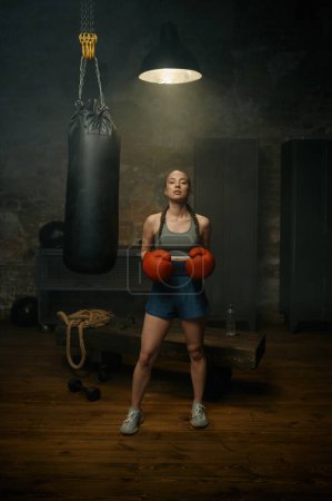 Photo for Portrait of beautiful sportive woman in red boxing gloves posing in gym studio - Royalty Free Image