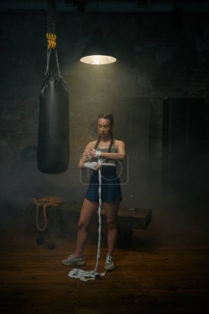 Photo for Strong woman athlete wrapping her hands with boxing bandages. Female boxer preparing for practicing fighting exercise and kickboxing - Royalty Free Image