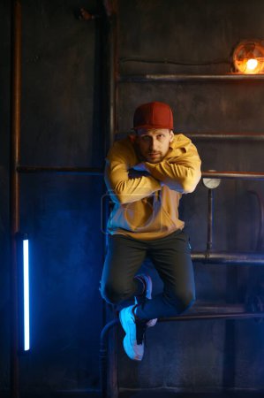 Téléchargez les photos : Hipster breakdancer portant des vêtements décontractés posant pour caméra sur fond de métro souterrain loft. Portrait du danseur hip hop B-boy - en image libre de droit